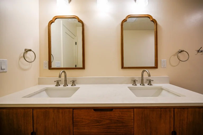 Remodeled primary bathroom in Ann Arbor with a walnut double vanity, white quartz top, brushed nickel cross-handle faucets and two arched wood mirrors