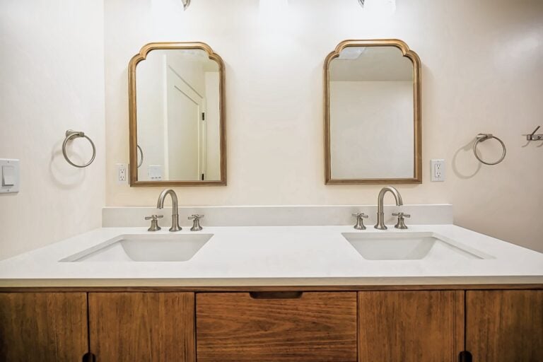 Remodeled primary bathroom in Ann Arbor with a walnut double vanity, white quartz top, brushed nickel cross-handle faucets and two arched wood mirrors