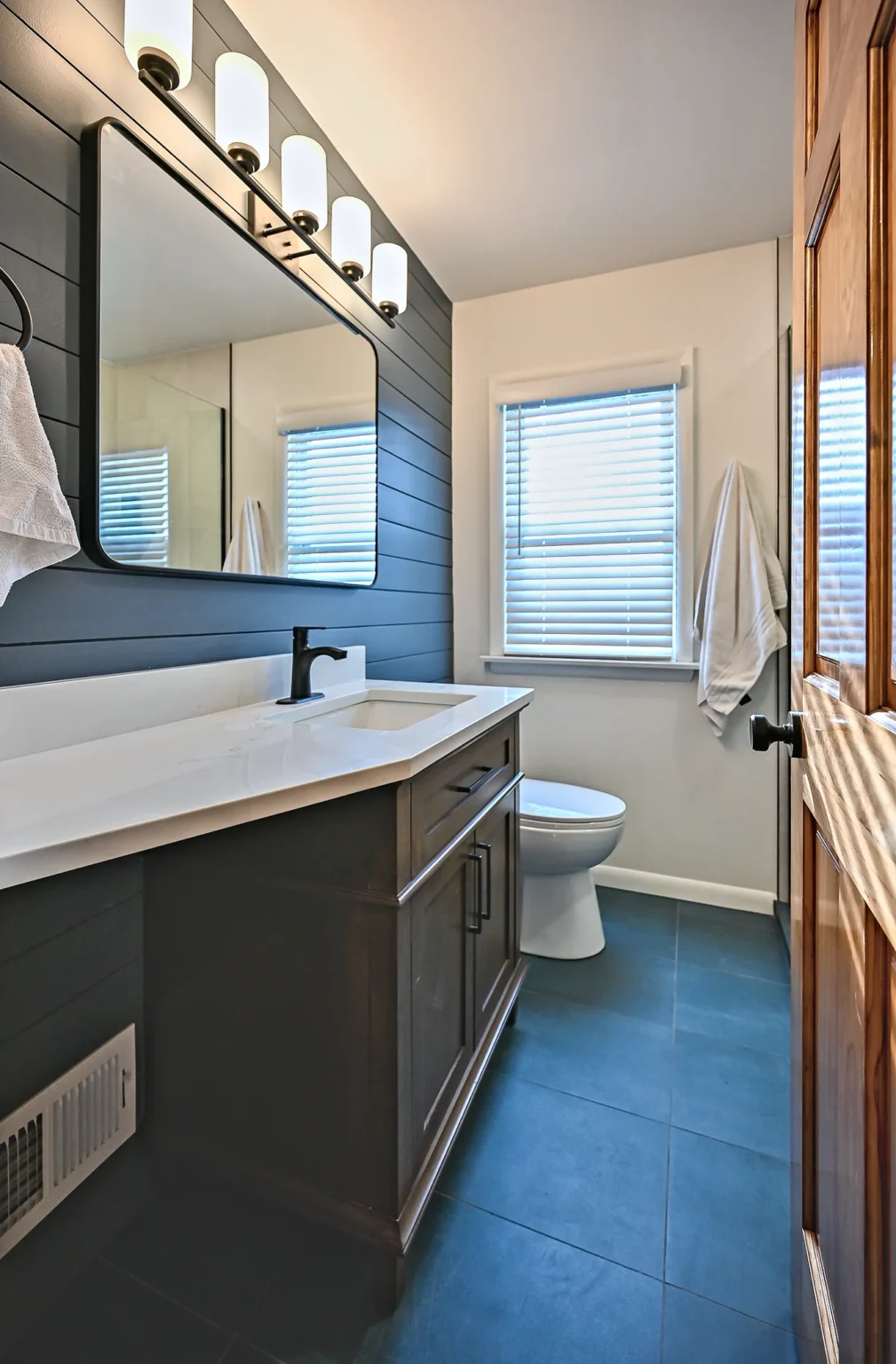Remodeled primary bathroom in Ann Arbor with a navy shiplap wall, dark wood vanity, white quartz top and charcoal tile floor