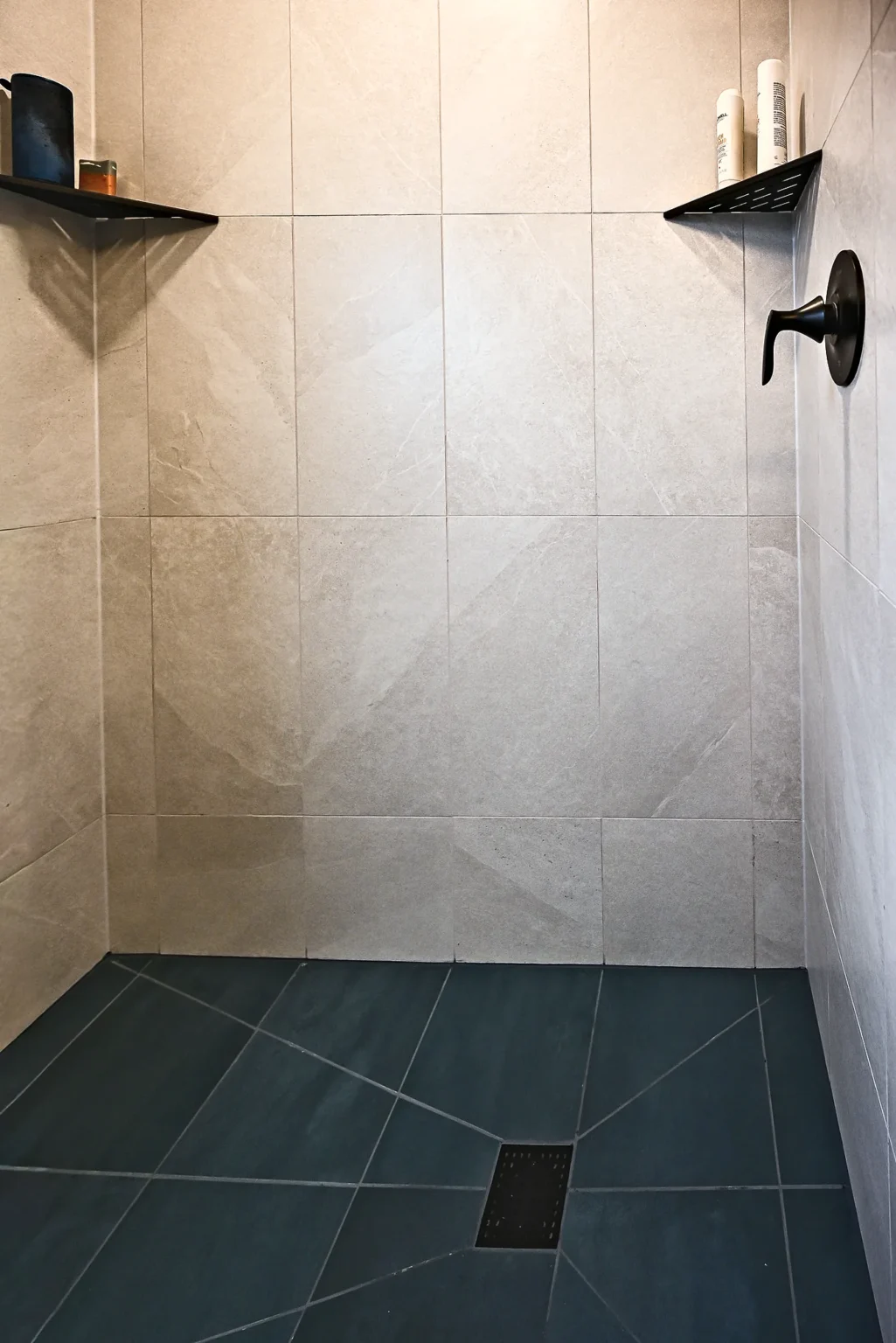 Shower floor in charcoal porcelain tile with a square matte black drain and cream wall tile
