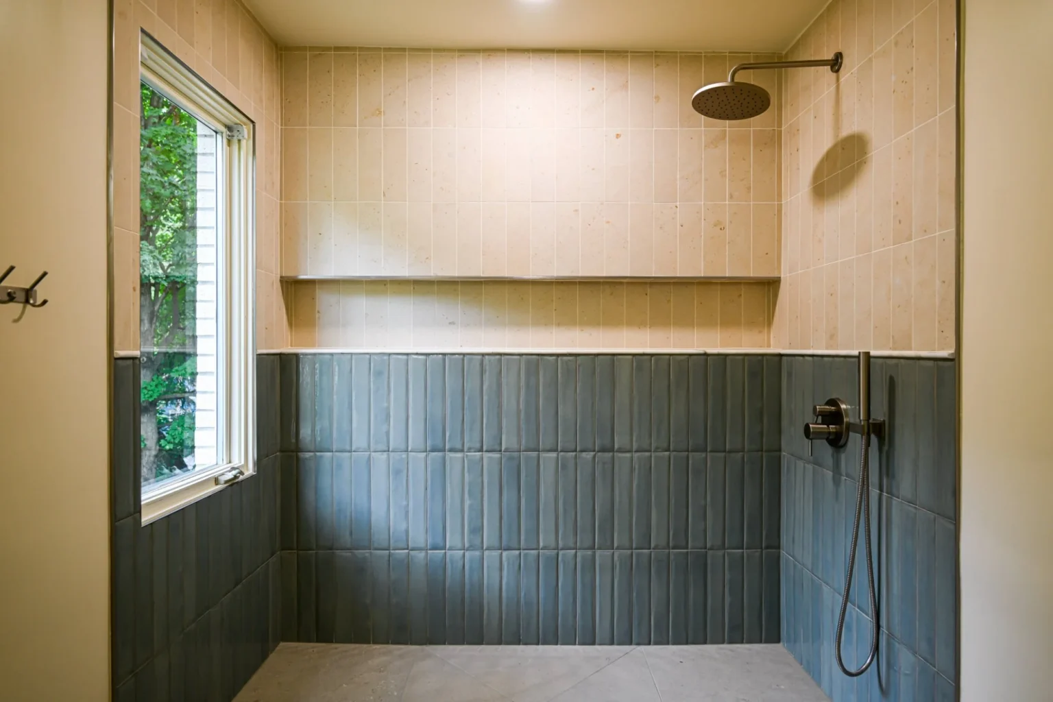 Shower wall with a brushed nickel rain head, handheld sprayer on a slide bar and a full-width tile ledge above blue vertical tile
