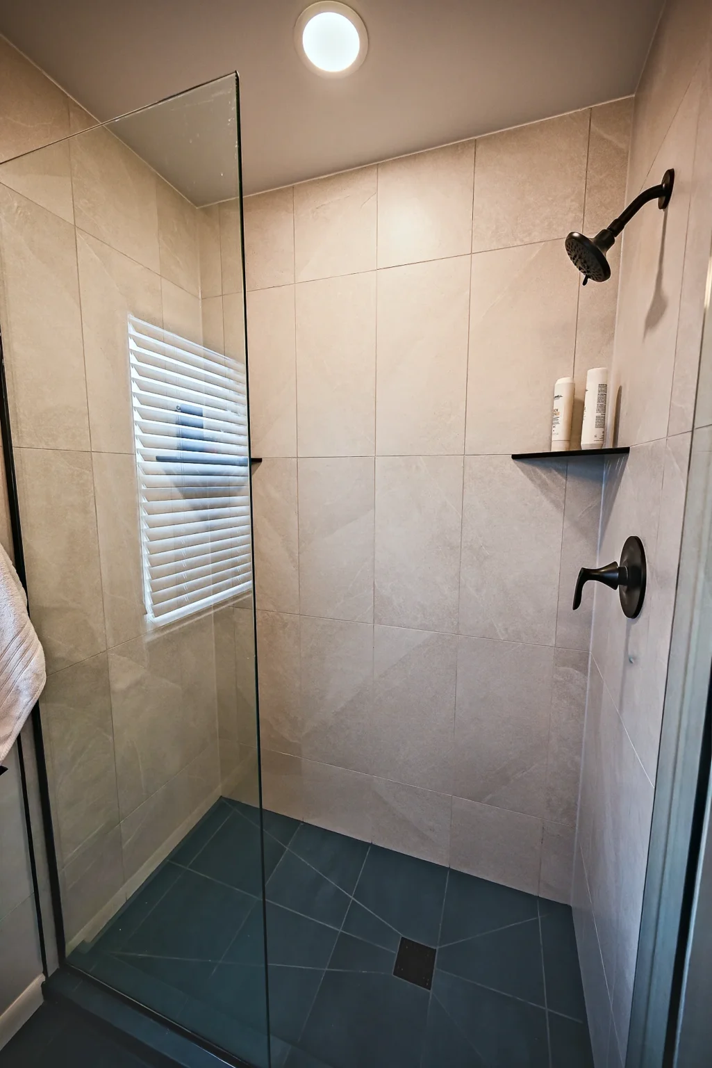 Walk-in shower with cream porcelain wall tile, a matte black rain head and corner shelves