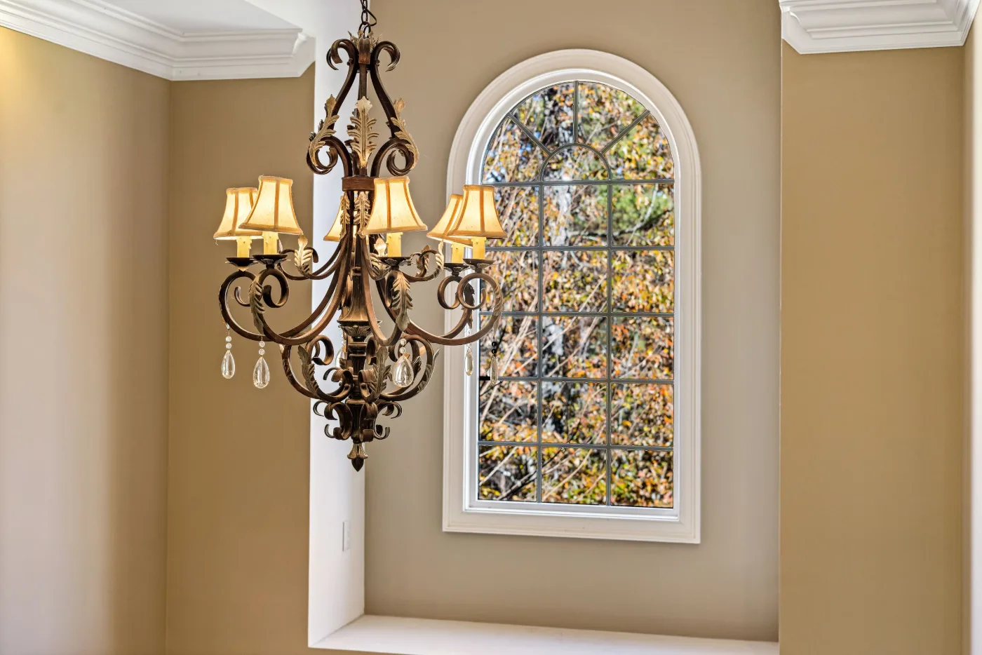 Arched window with grilles above a deep sill in a tan dining room with a chandelier