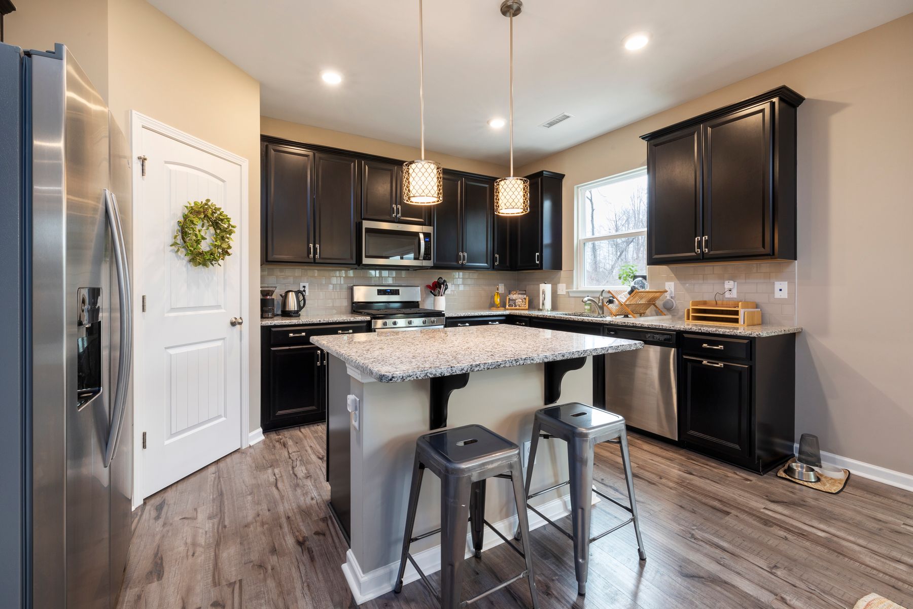 Kitchen with black cabinets, a granite island and two metal stools