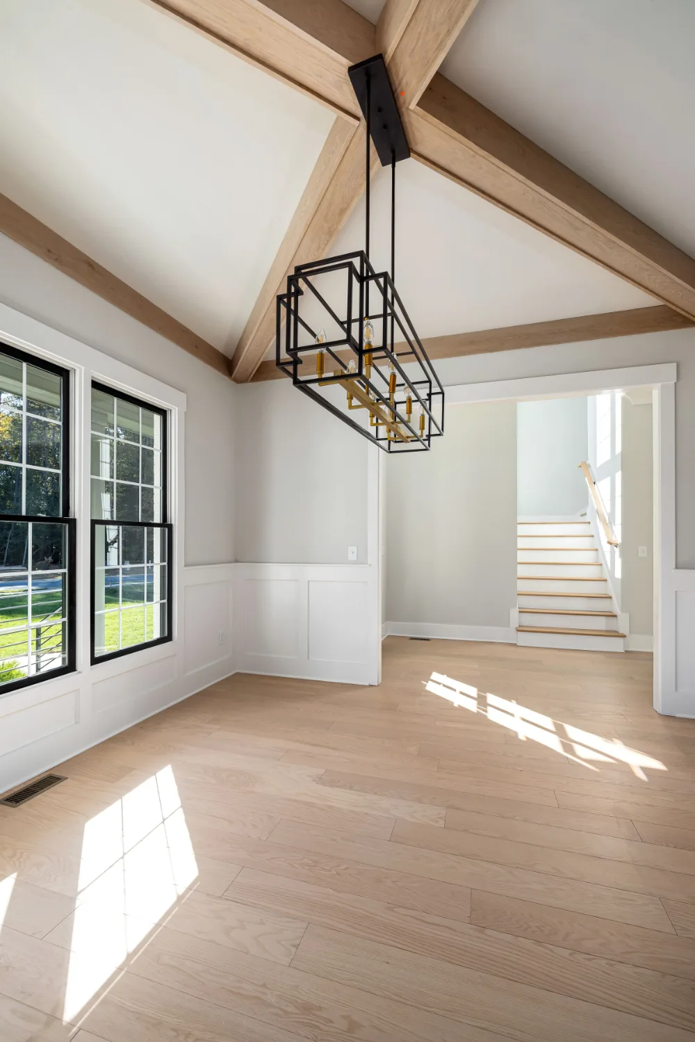 Black-framed windows along the wall of a vaulted room with exposed beams and light oak floors