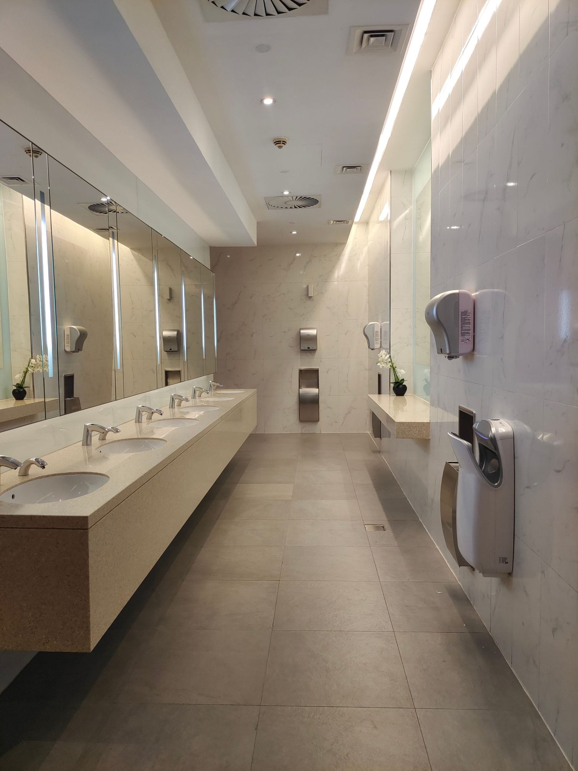 Long stone vanity with undermount sinks and wall mirrors in a bright commercial restroom