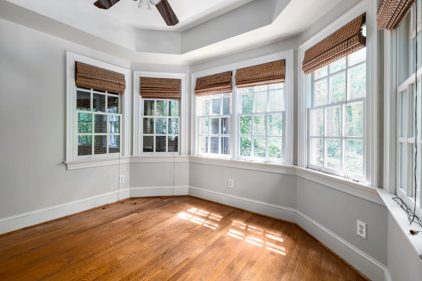Row of white double-hung windows wrapping a corner of an empty room with woven shades