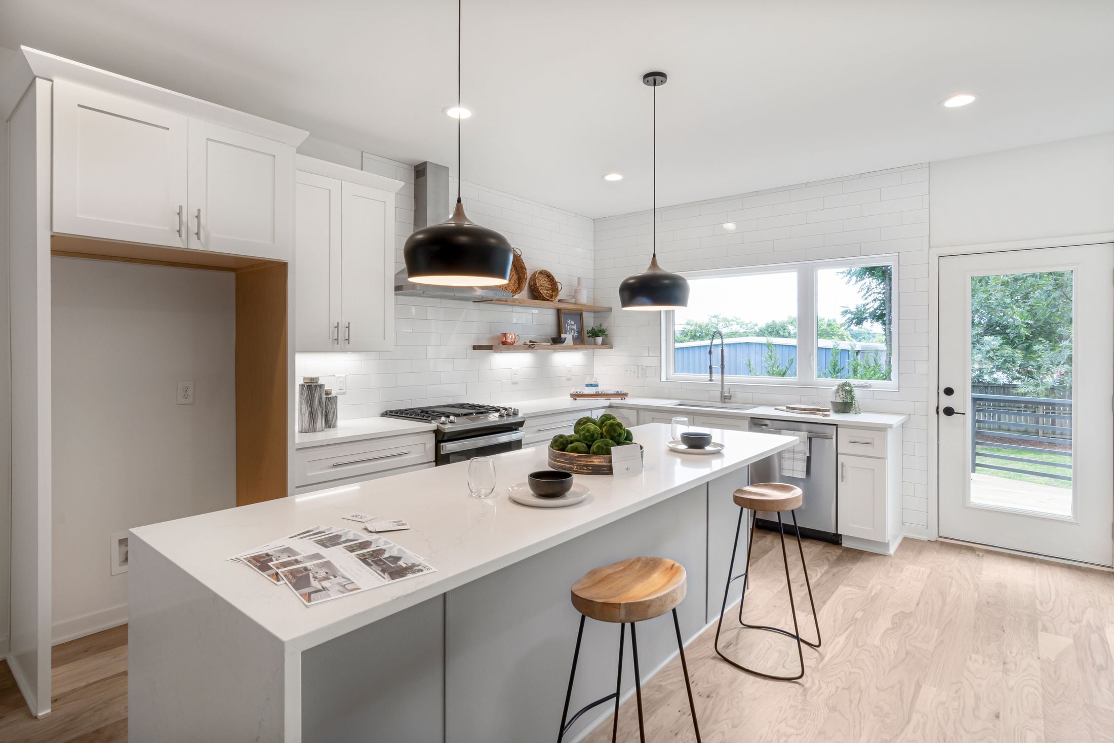 White kitchen island with black pendants and stools, open to a glass door and the backyard
