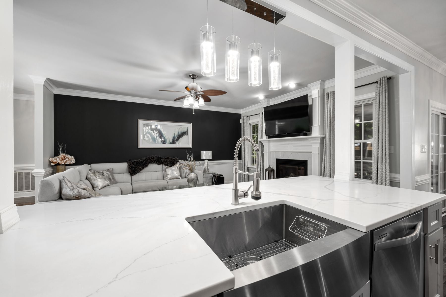 Stainless undermount sink set into a white island, looking across to a living room with a dark accent wall