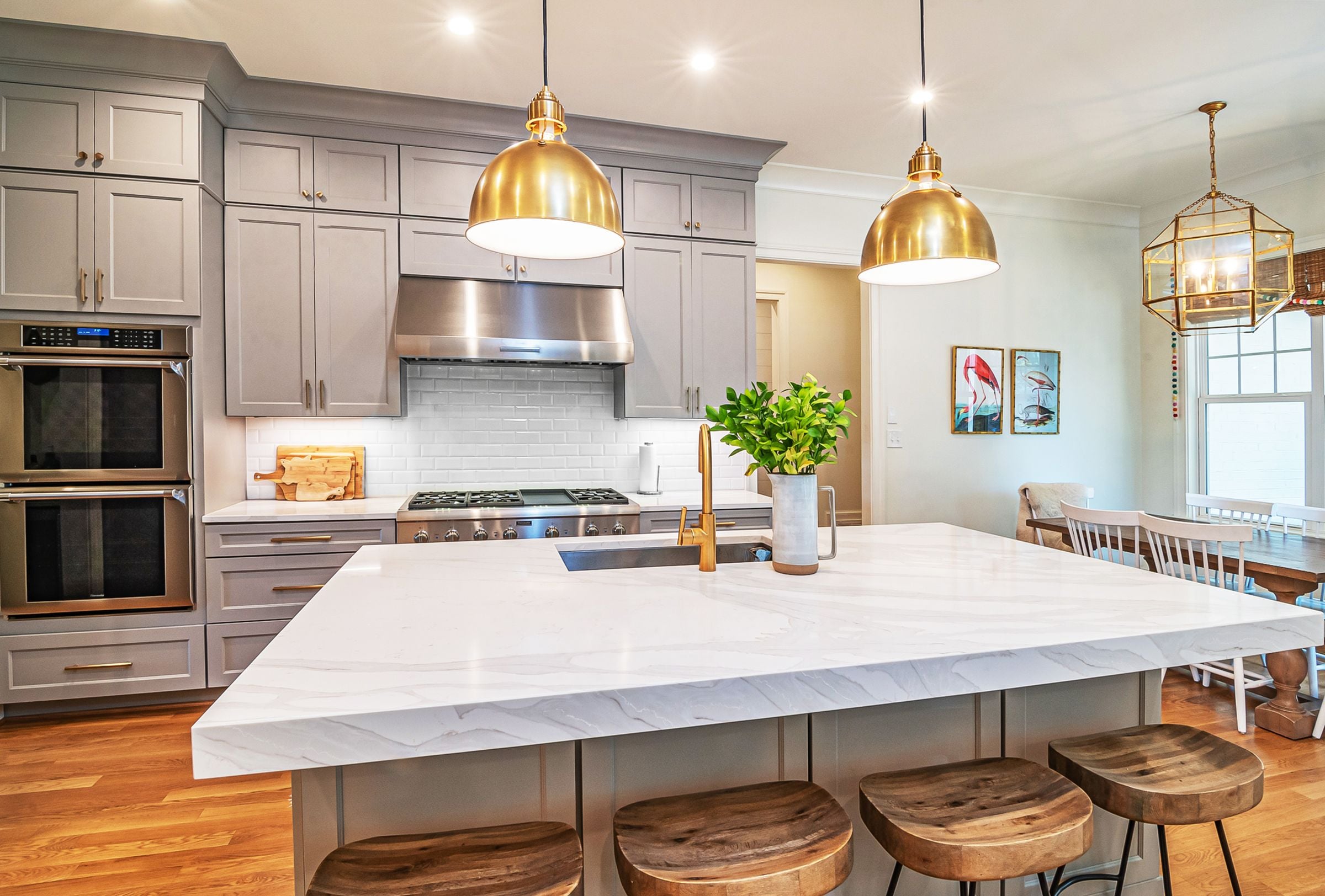 Marble-topped island under three gold pendant lights in a gray and white kitchen