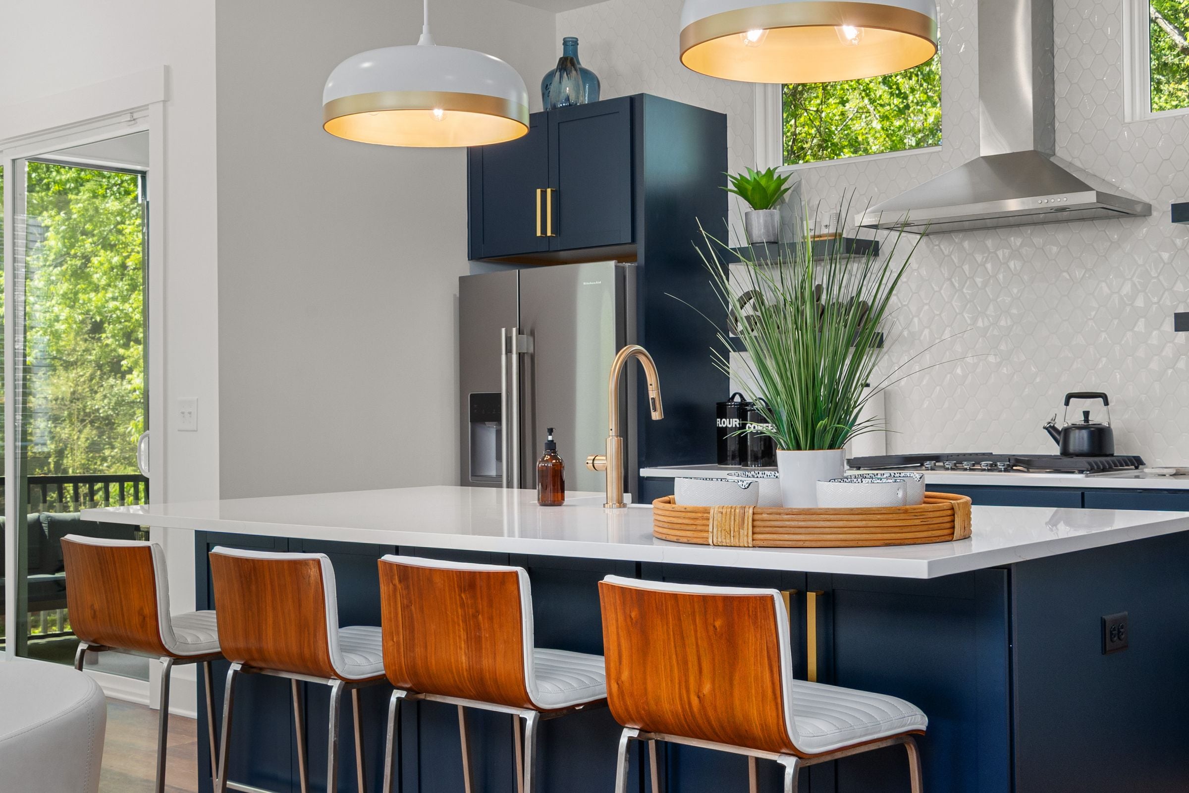 Navy kitchen island with a white quartz top, wood and leather stools, a brass faucet and a single pendant