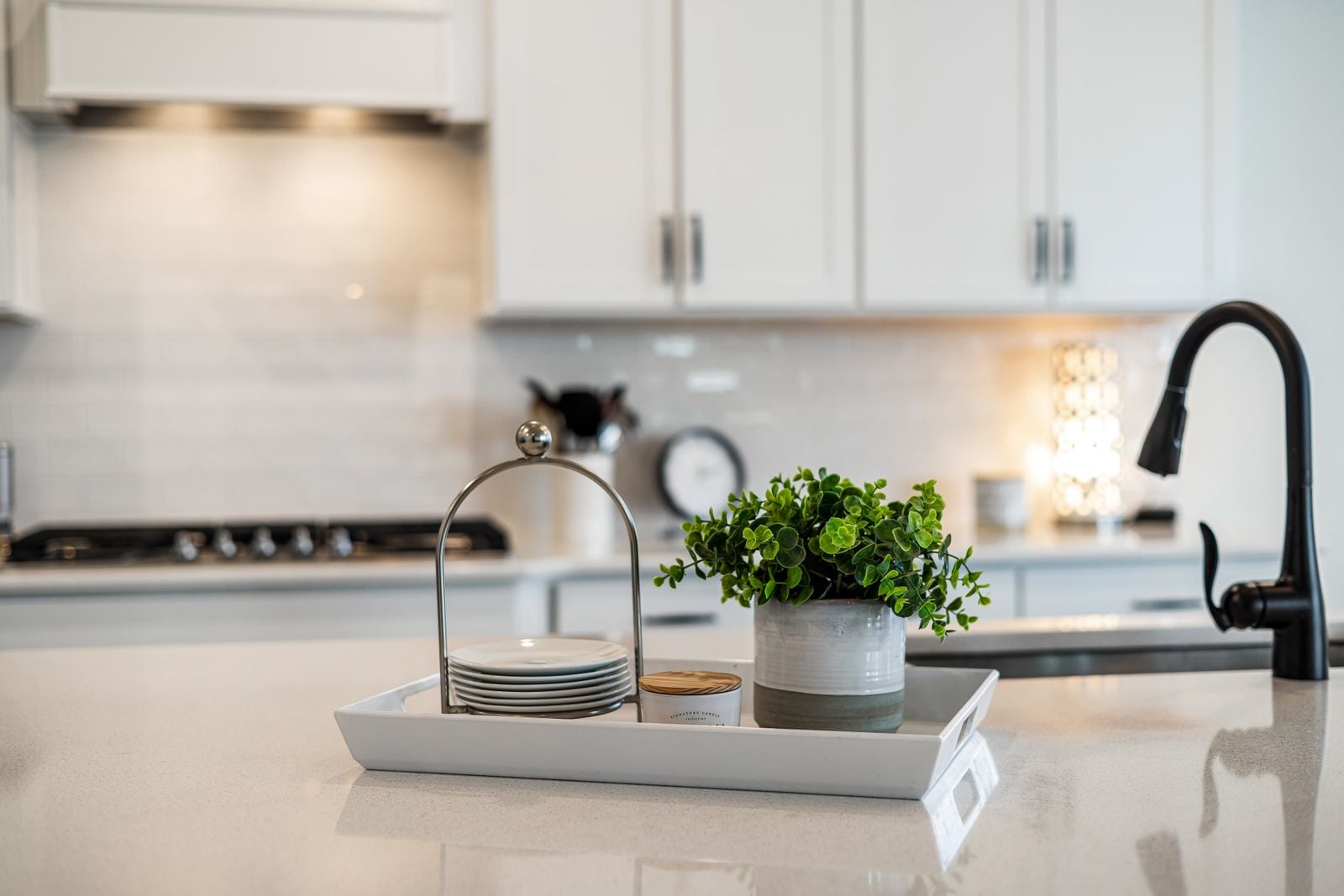 Close view of a white kitchen counter with a matte black faucet, a potted plant and a stack of plates