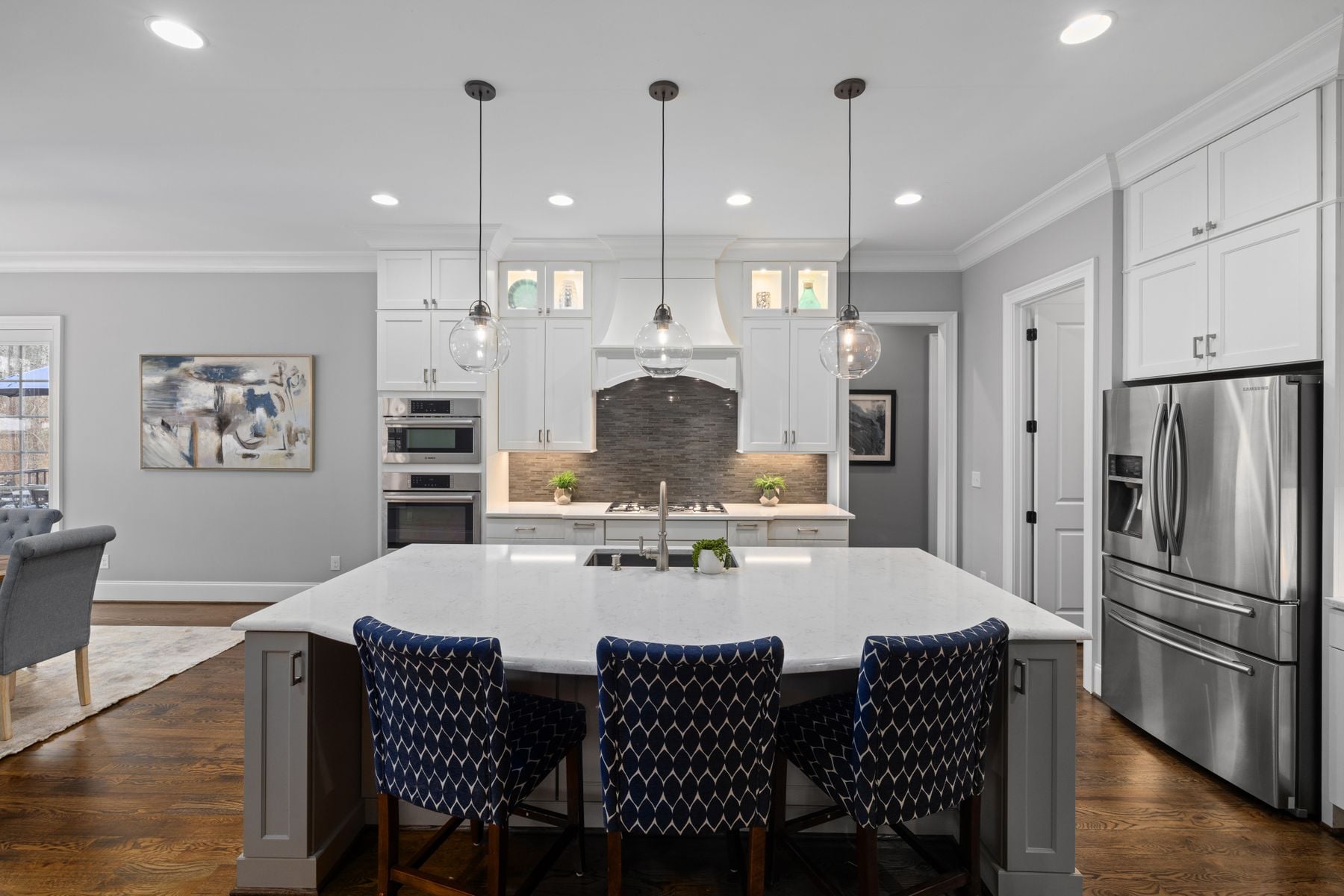 White kitchen island with four navy upholstered stools under two pendants