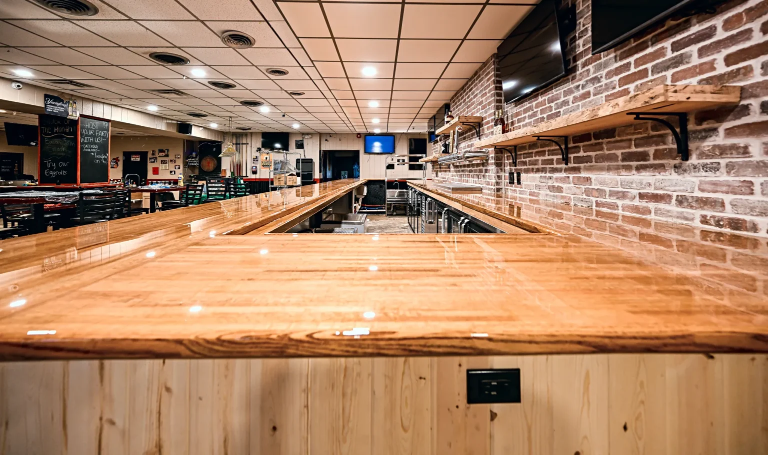 Looking down the sealed butcher block bar top toward the dining room of 342 Bar and Grill, with the brick back bar and live-edge shelves on the right