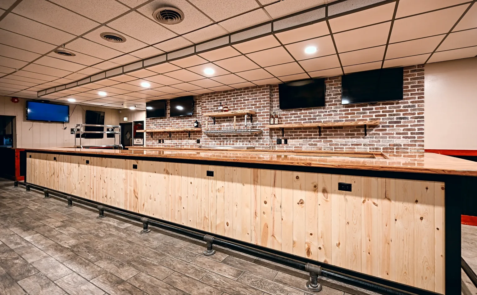 Remodeled commercial bar in Dearborn Heights with a knotty pine front, butcher block top, black iron foot rail and a brick back bar with live-edge shelves