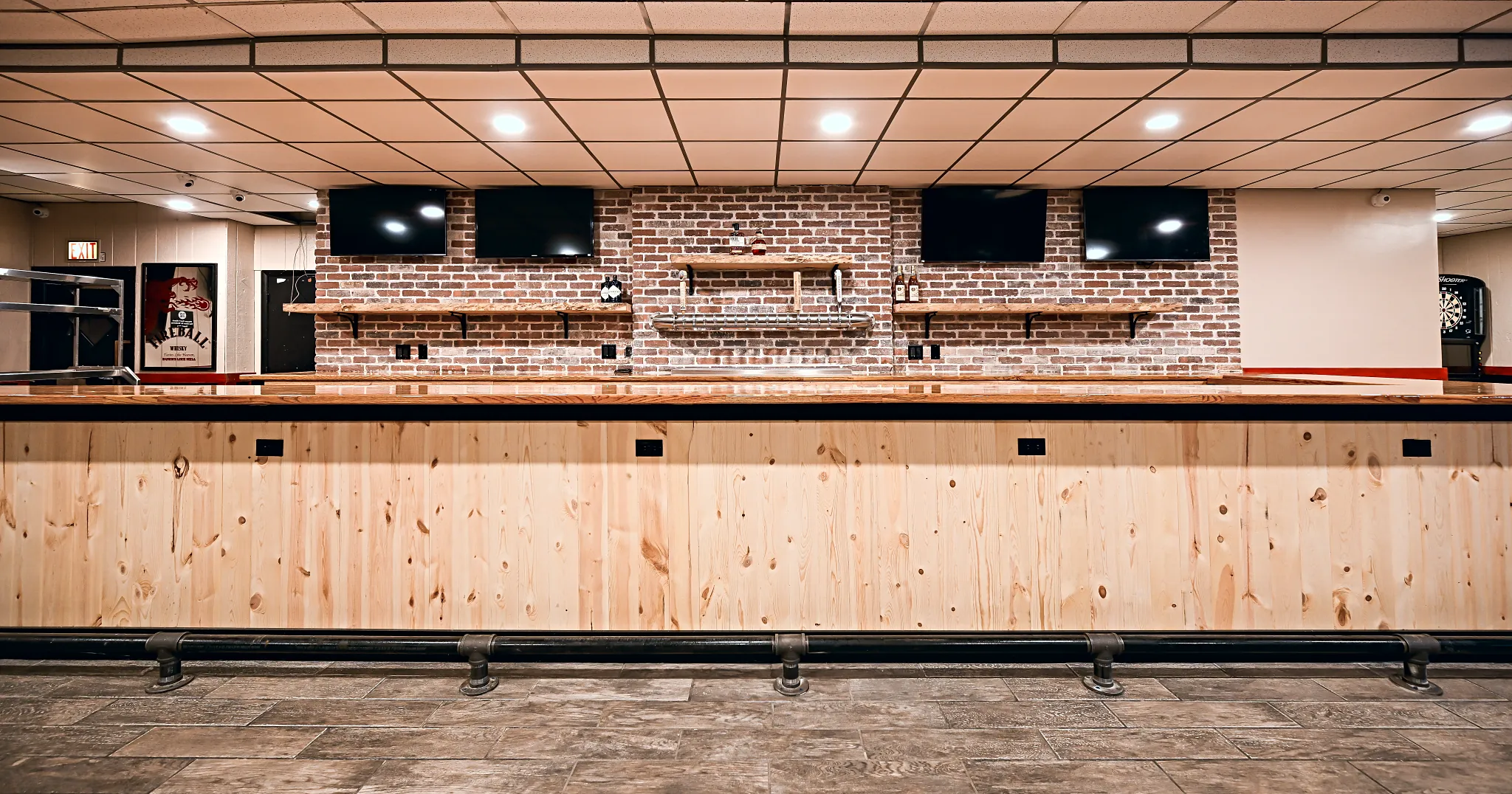 Straight-on view of the remodeled bar at 342 Bar and Grill in Dearborn Heights: knotty pine front, butcher block top, black foot rail and a brick back bar with four televisions and live-edge shelves