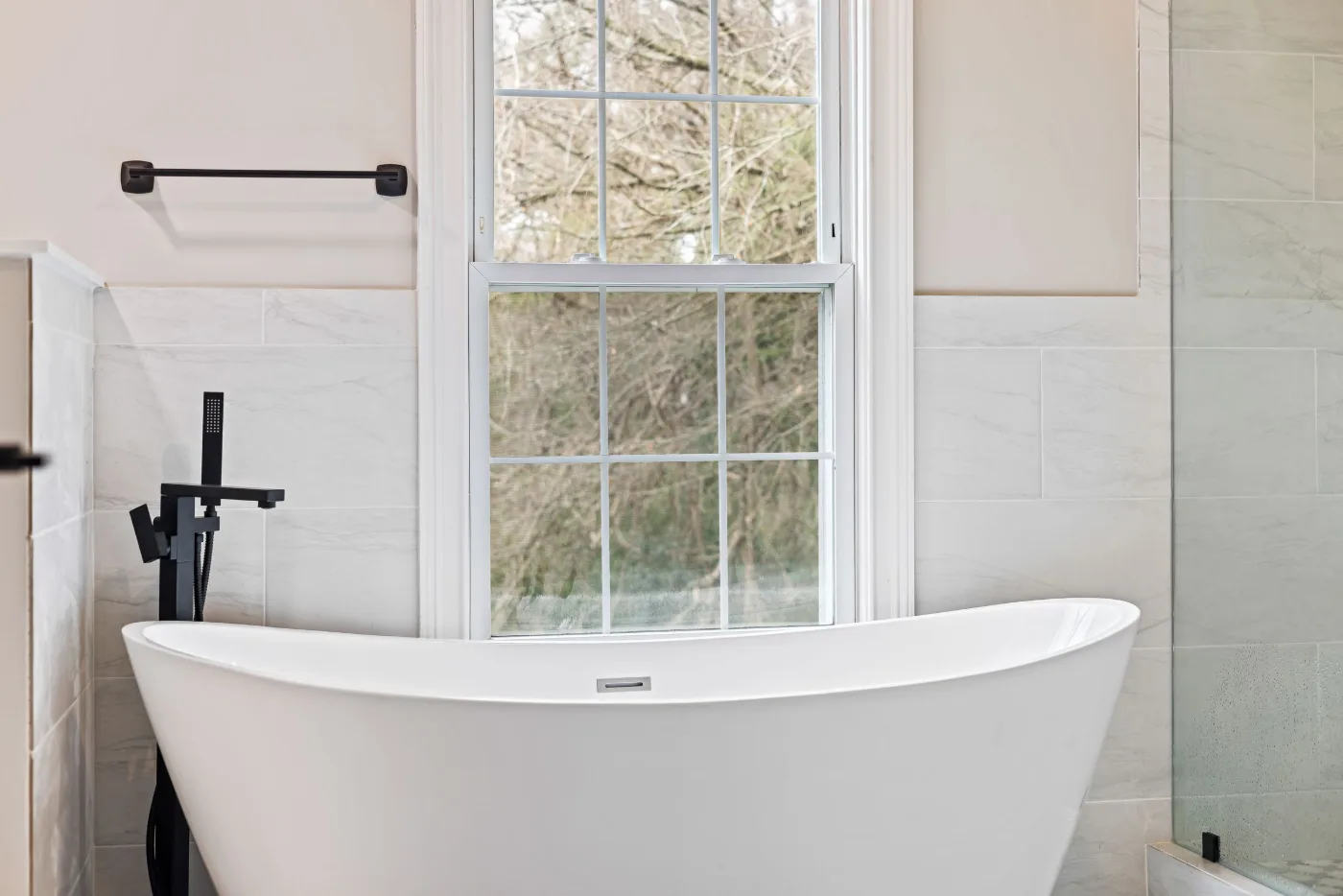 White double-hung window with grilles above a freestanding tub in a tiled bathroom