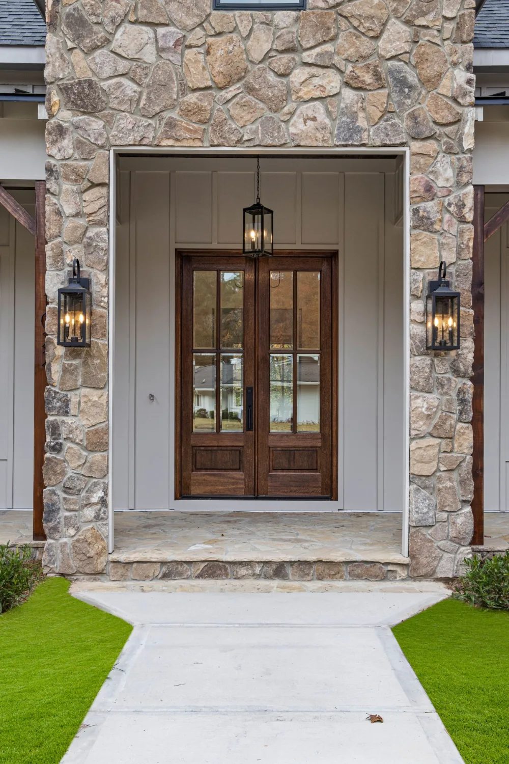 Pair of wood and glass double entry doors framed by stone columns and black lanterns