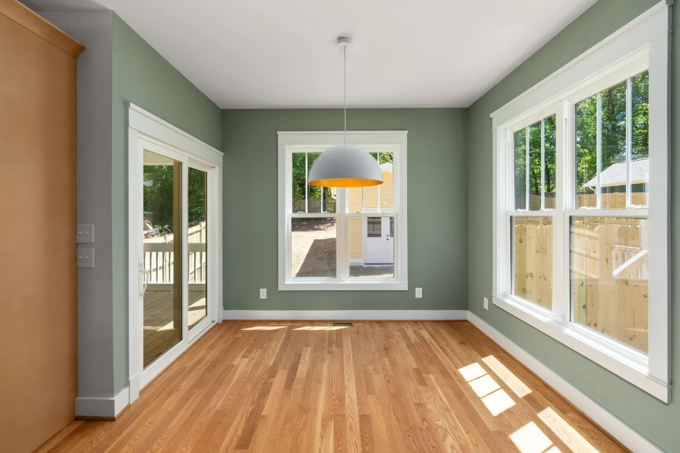 Empty room with sage green walls, white window trim and hardwood floors