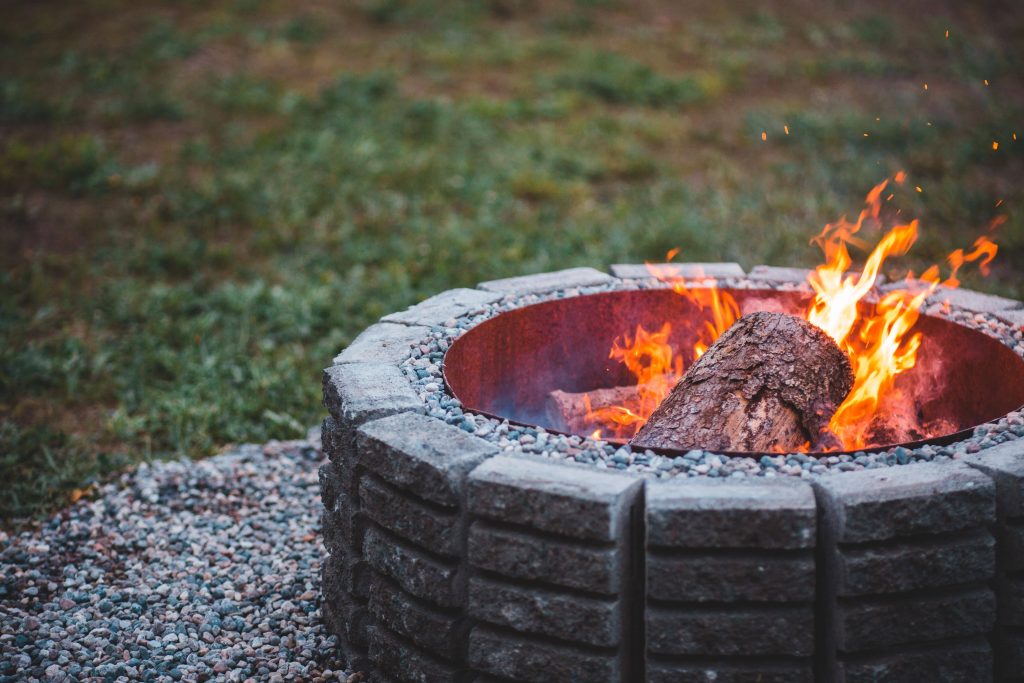 Round stacked stone fire pit with logs burning on a gravel patio