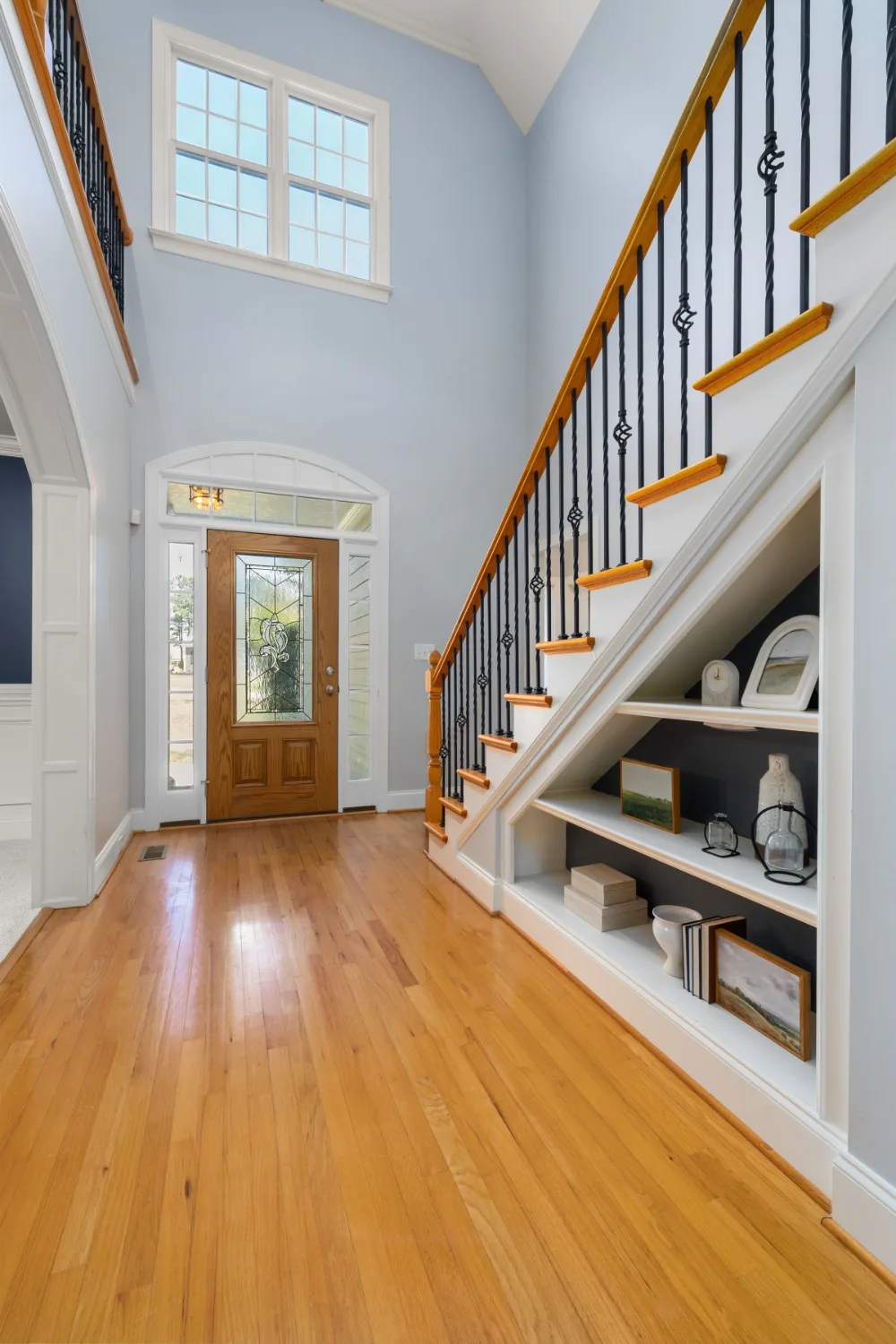 Two-story foyer with a wood front door, a glass sidelight and a staircase with black balusters