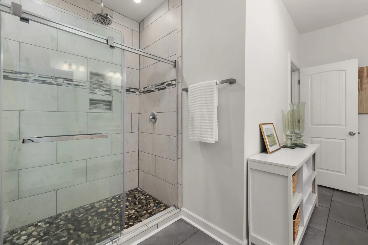 Glass walk-in shower with tiled walls and a pebble stone floor