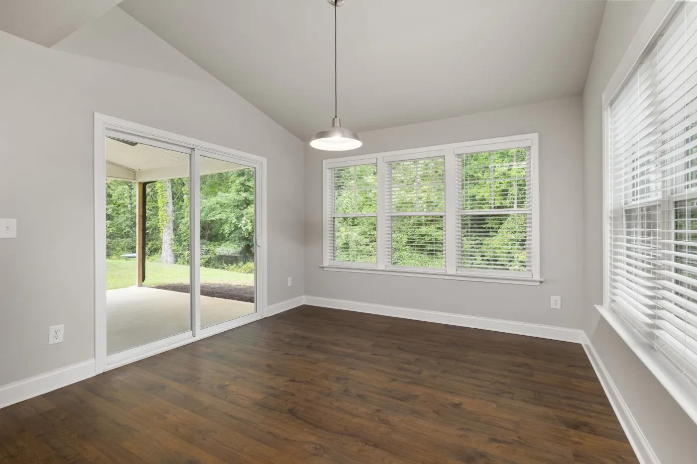 Empty sunroom with a sliding glass patio door, a bank of double-hung windows and dark wood floors