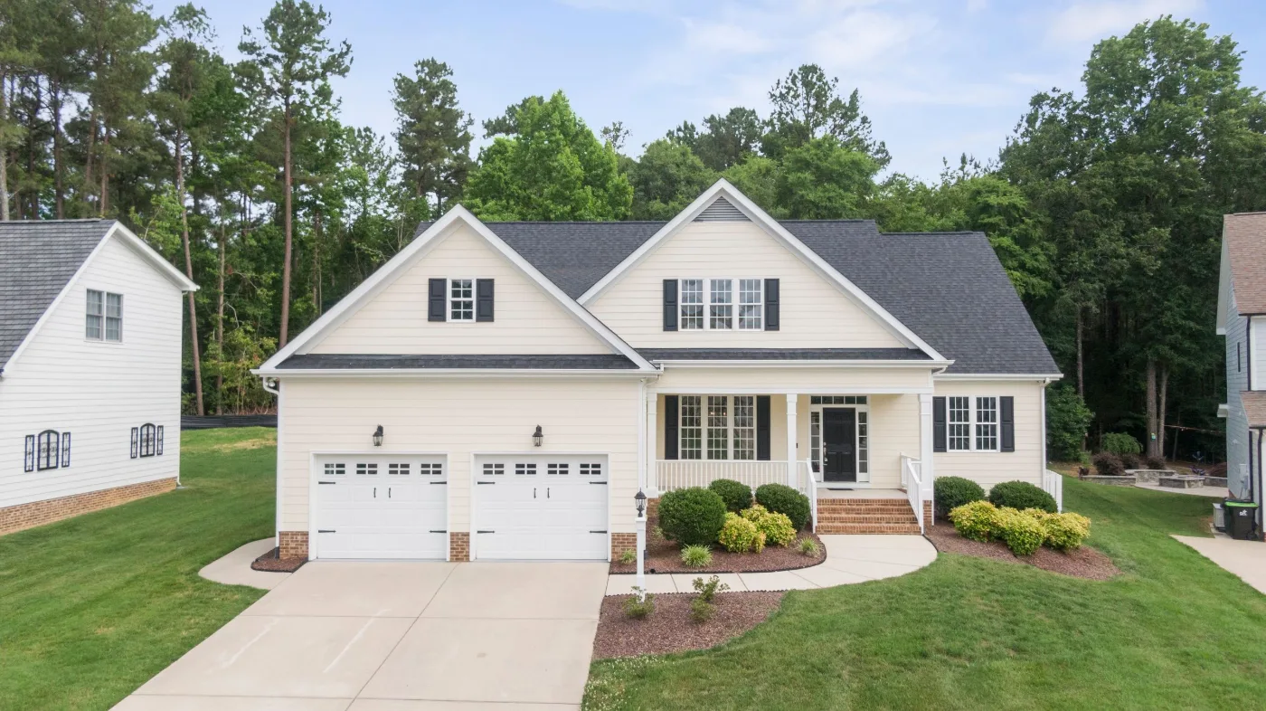 Two-story white house with a two-car garage, black shutters and a wooded backyard