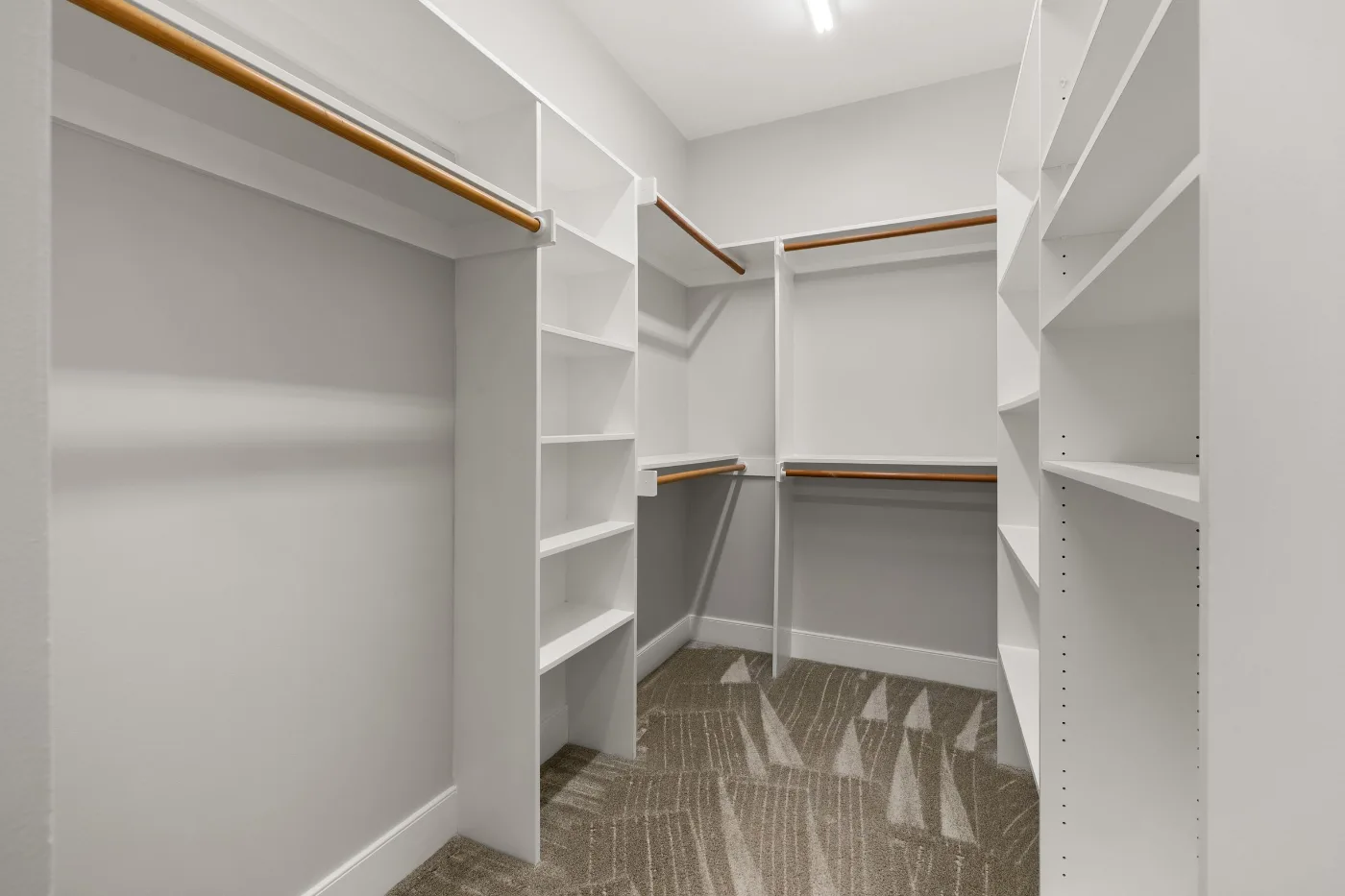 Empty walk-in closet with white shelving and wood hanging rods