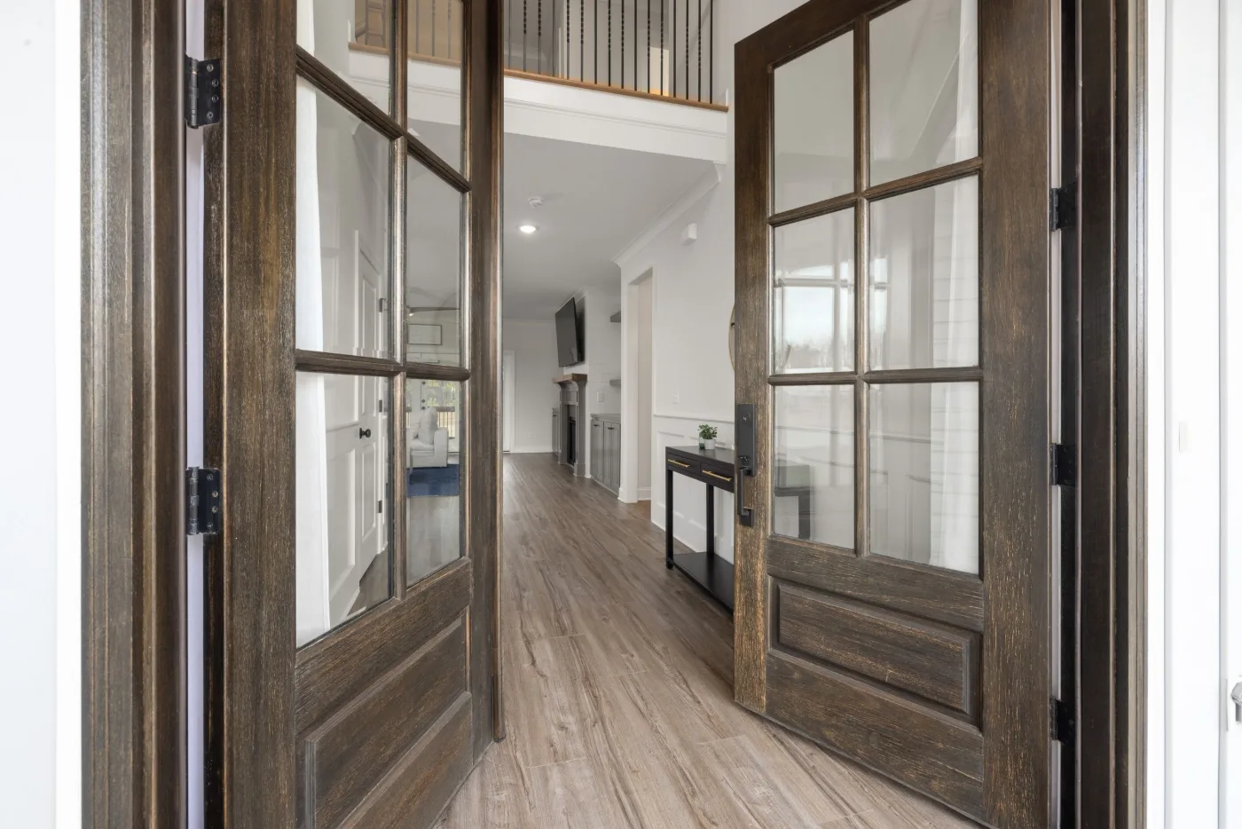 Open pair of dark wood French doors with full glass panels leading to a hallway