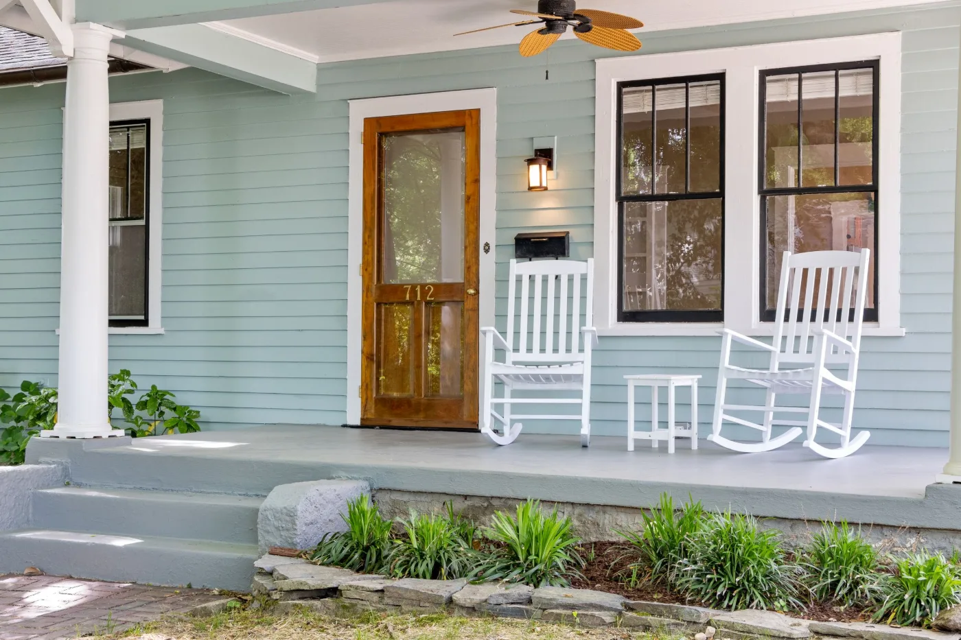 Wood and glass front door on a light blue porch with two white rocking chairs