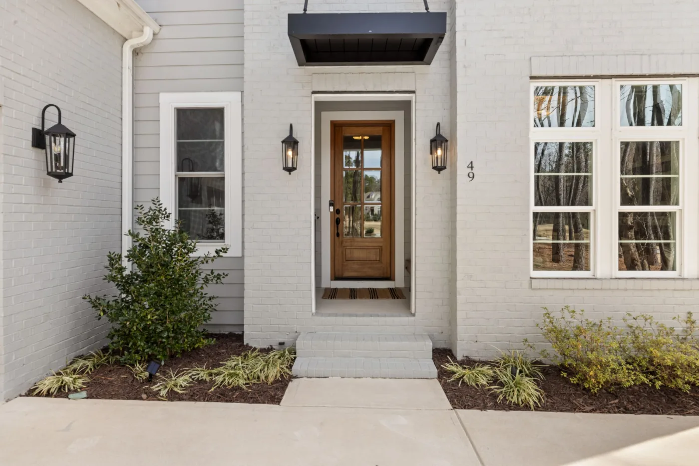Narrow wood front door with glass panels set in gray lap siding between two wall lanterns