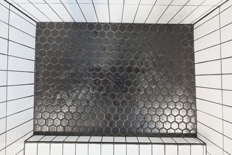 Looking down into a shower at a black hexagon mosaic floor framed by white vertical wall tile